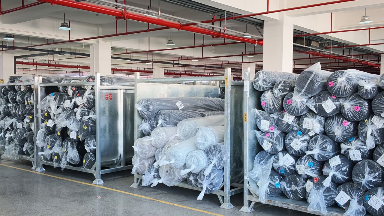 Fabric rolls wrapped in plastic on metal racks in the warehouse / 面料库房实拍：金属货架上的成卷面料